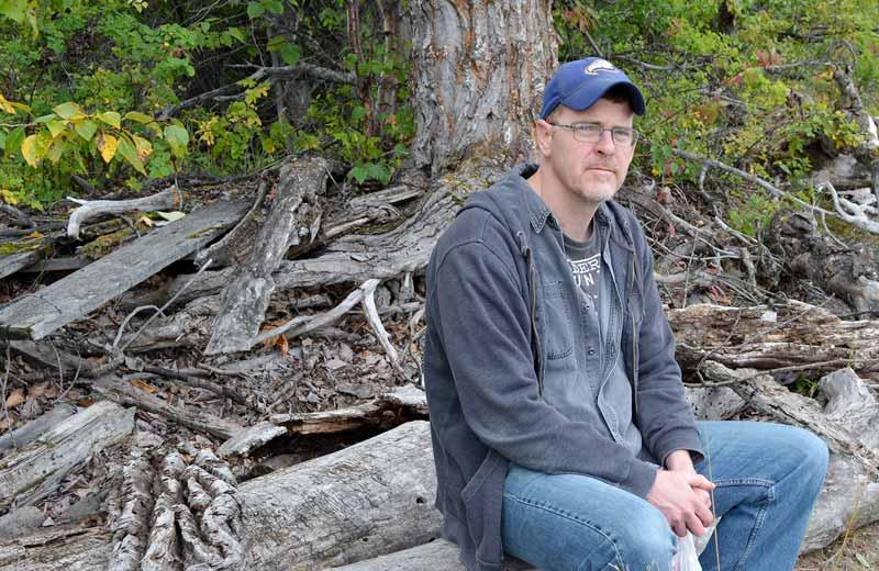 A man sits on a log and looks into the camera.