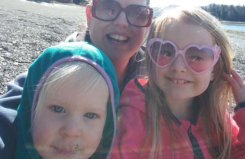 A woman in sunglasses and two children taking a selfie on a beach.