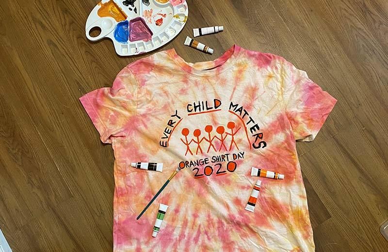 A tie-dye orange t-shirt decorated with paints for Orange Shirt Day 2020.