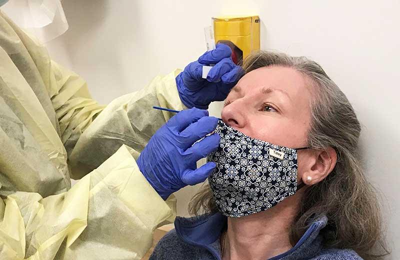Woman in mask receives nasal swab test by nurse in gown.