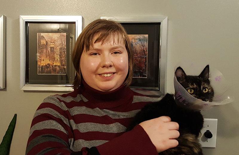 Woman smiles at camera while holding a black cat