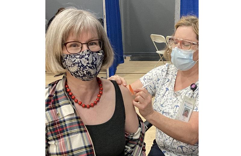 Woman wearing a mask receives a vaccine from a nurse