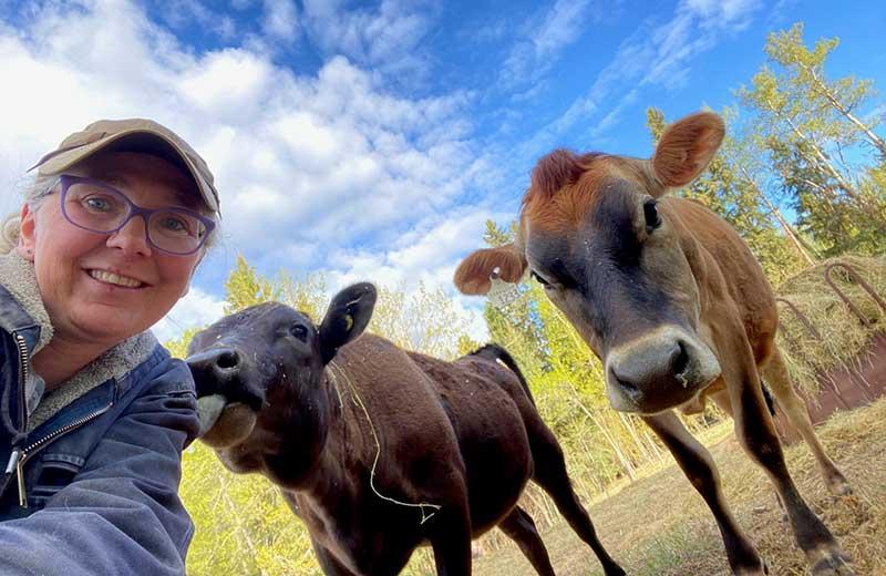 Woman with a hat poses for selfie with 2 cows