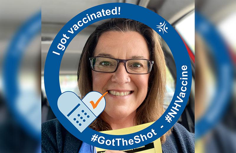 Woman smiling holding her vaccination card with Northern Health COVID-19 vaccination graphic.