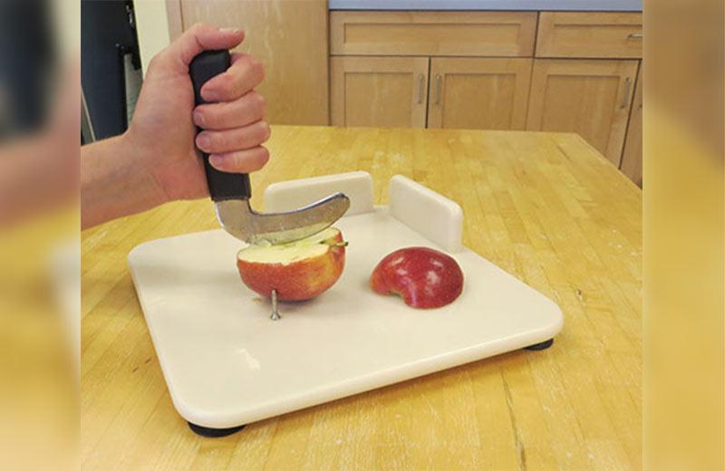 Person cutting an apple on a white cutting board with one hand.