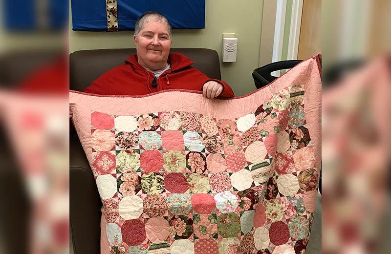Smiling woman holding up a pink quilt.