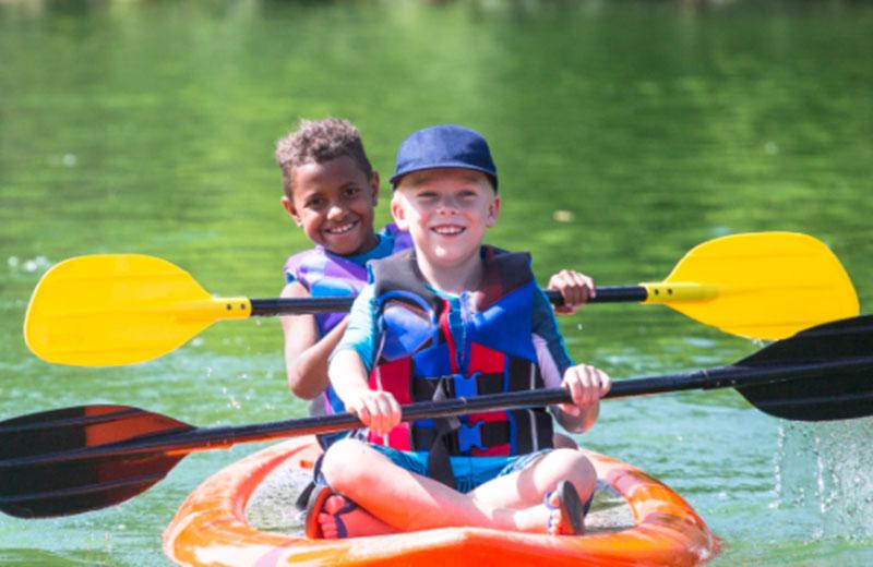 Two young children paddle in a kayak on the water.