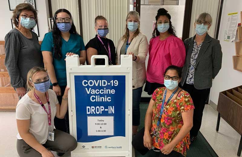 Group of women wearing masks stand next to a COVID-19 clinic sign