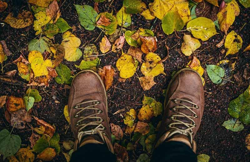 Brown boots on dirt trail with yellow leaves.