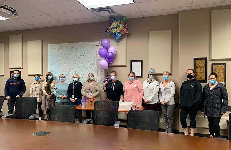 A group of people stand in a line wearing masks to celebrate the one year anniversary of the virtual clinic
