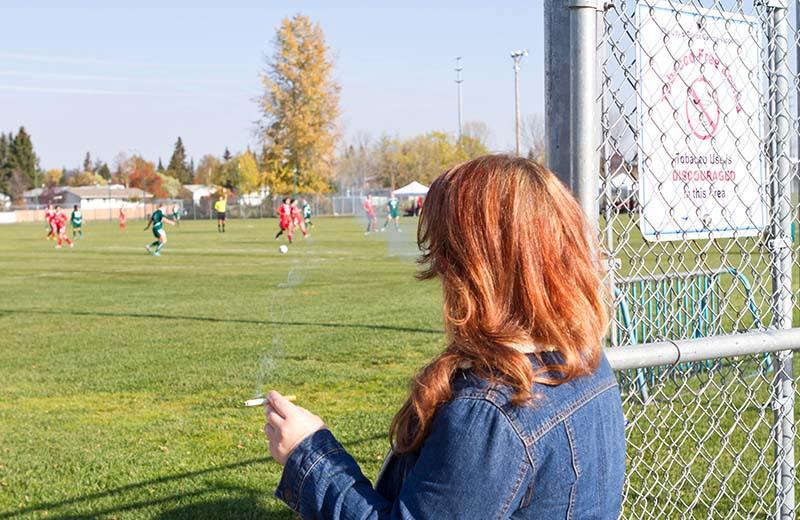 a woman with red hair watched children play on a field with a cigarette in her hand