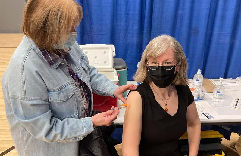 a nurse is shown administering a vaccine to the arm of a woman with shoulder length grey hair