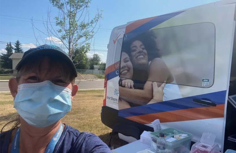 Woman wearing a mask stands in front of a health care van