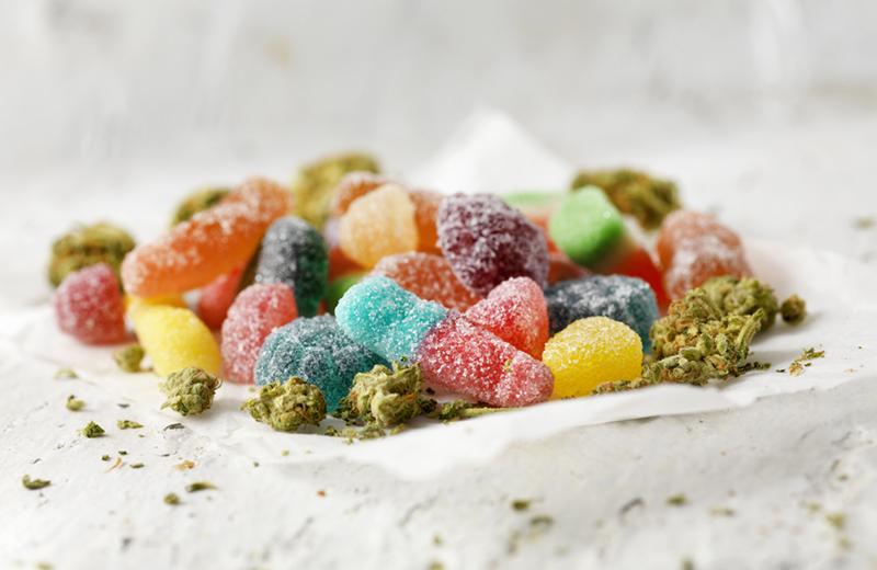 a pile of rainbow gummies with cannabis bud sprinkled over it