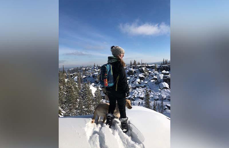 Backpacker stands on snowy hill with dog