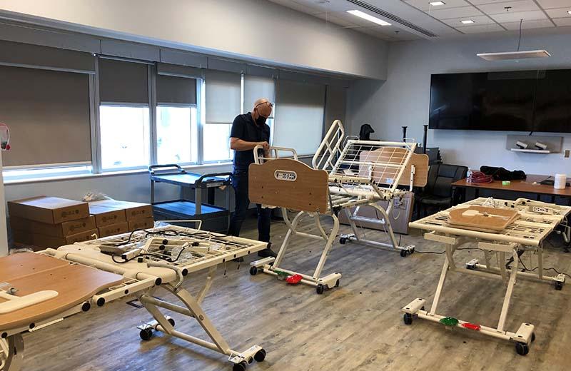 a man stands in the centre of the room assembling hospital beds 