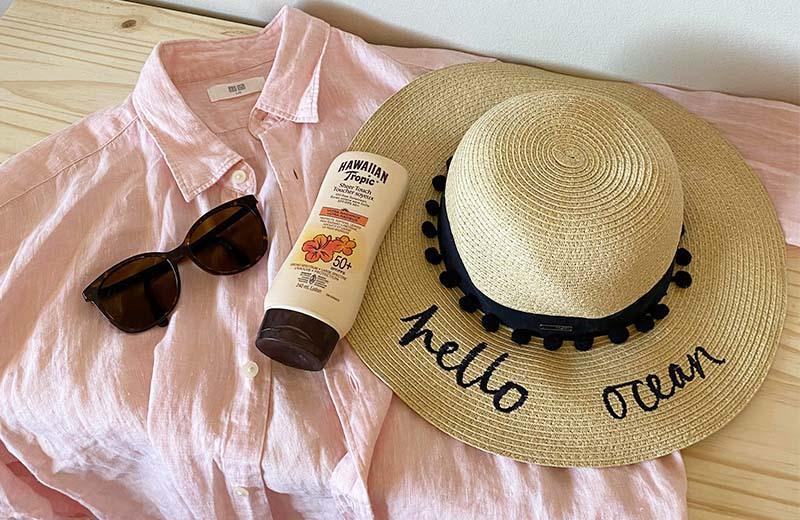 a hat, bottle of sunscreen, sunglasses, and linen shirt are laid out on a table.
