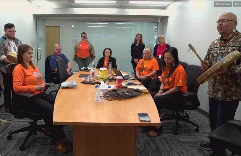 a group of people wearing orange shirts sit around a board room table