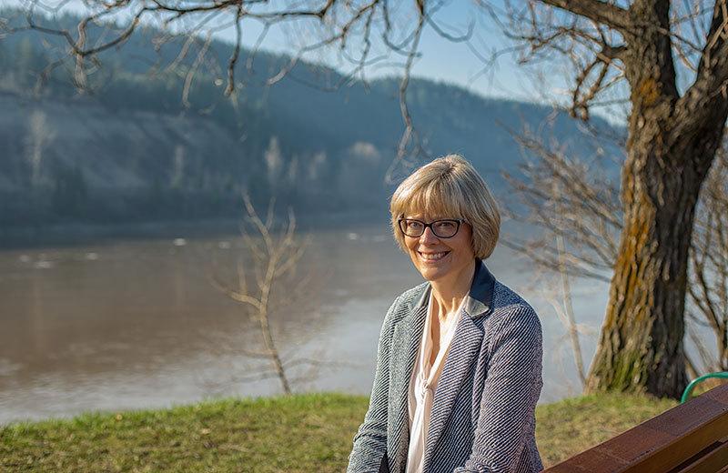 CEO Cathy Ulrich sits smiling on a bench at the Nechako river