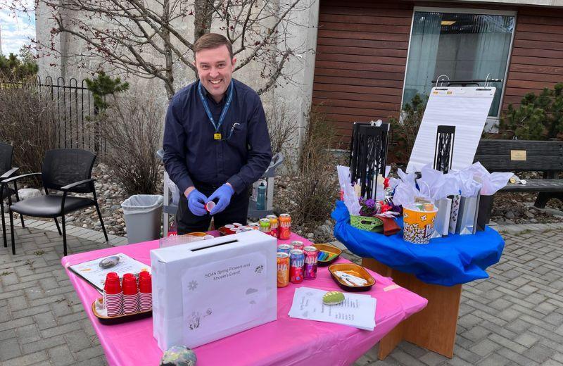 A man stands behind a table set with canned drinks, raffle entry box, and door prizes