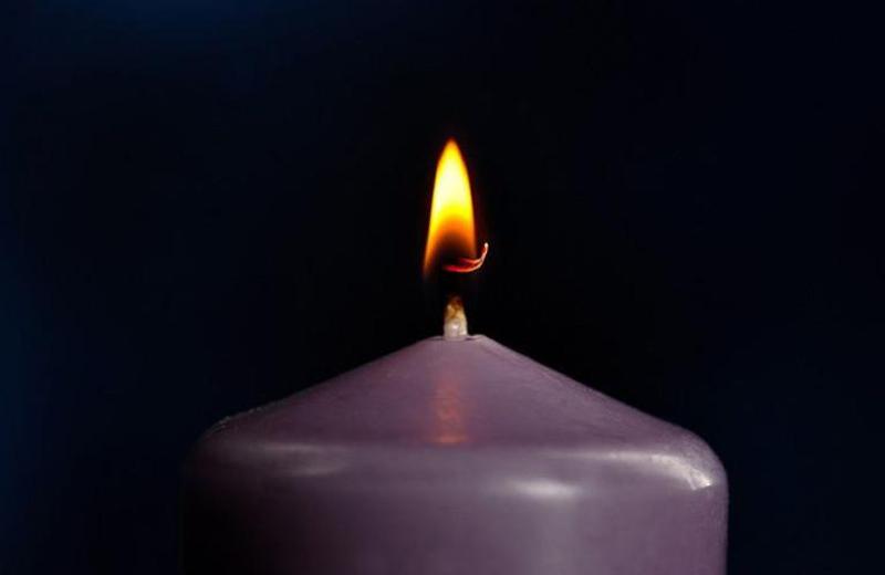 Purple candle with flame in front of a dark background.