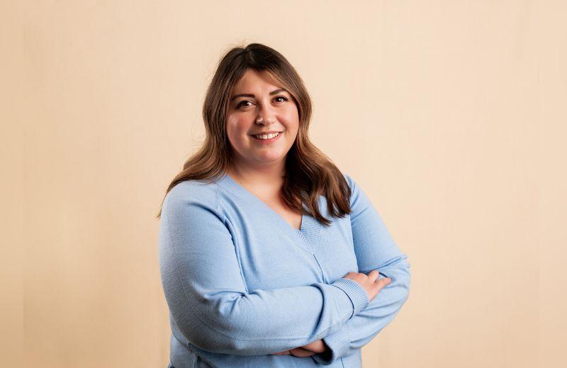 Lyndsey Rhea posing in a blue shirt against an orange background