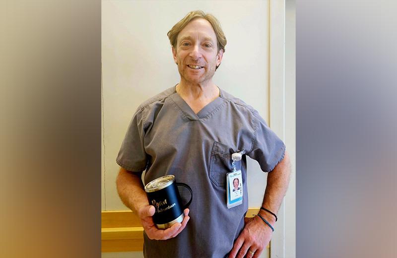 Male nurse stand in hallway holding an engraved cup