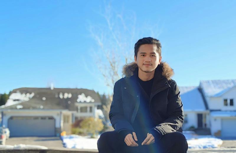 Man wearing a winter coat sits outside on a curb on a cold, clear sky day