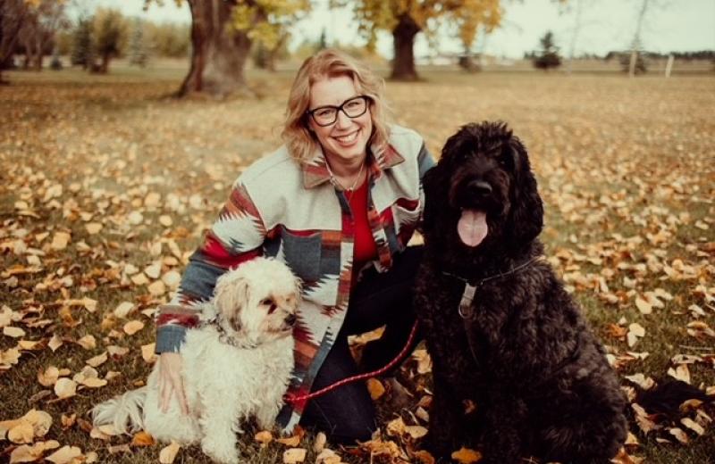 Woman poses with her dogs and the ground is covered in leaves.