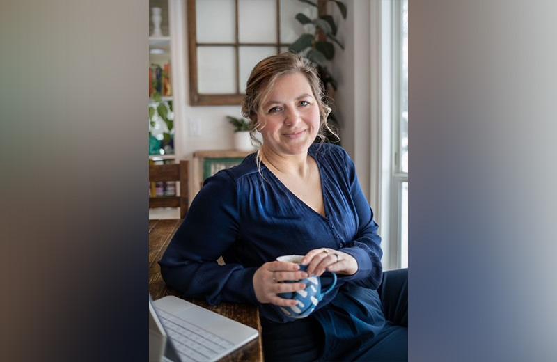 Woman sits in front of her laptop holding a mug of tea.