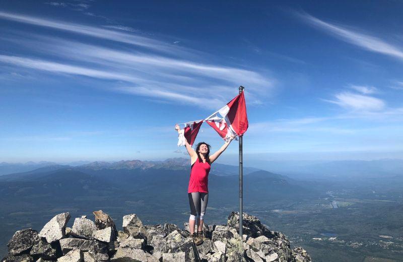 Savana standing atop a mountain holding onto a torn Canadian flag above her head