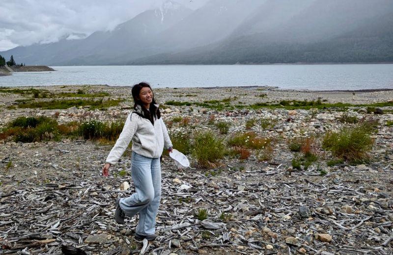 Tiffannie walking over white beach wood set against a lake and mountains in the background