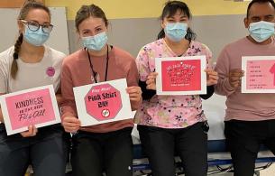 Nurses sit on a gurney holding anti-bullying, Pink Shirt Day signs 