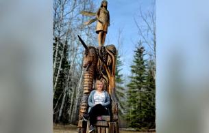 Darlene Danco sits on a chainsaw wood carving in Chetwynd BC. 