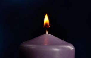 Purple candle with flame in front of a dark background.