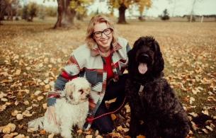 Woman poses with her dogs and the ground is covered in leaves.