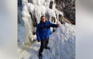 Penelope standing under a frozen waterfall wearing blue ice climbing gear