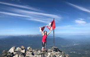 Savana standing atop a mountain holding onto a torn Canadian flag above her head