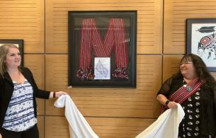 Kristen Scrivens and Bernadette Chaboyer standing beside a red, framed sash hung on the wall.