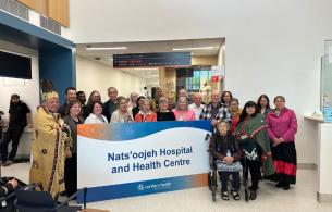 A large group of people stand holding a sign noting the name of the new hospital. 