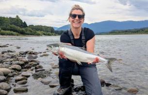 Amanda holding a freshly caught fish on the banks of a river